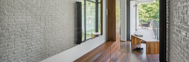 Dolne meble w przedpokoju z siedziskiem: panorama korytarza domowego z długim lustrem, białą ceglaną ścianą, drewnianą podłogą i ławką