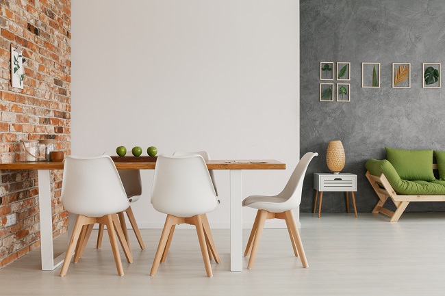 Drewniany stół i krzesła przy odsłoniętej ceglanej ścianie w jasnym i naturalnym wnętrzu salonu nowoczesnego loftu